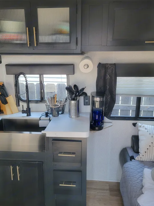 This modern RV rental interior features a sleek kitchen galley with black cabinets, sink, and a glimpse of the cozy sleeping area.. Forest River Cherokee Grey Wolf 2022