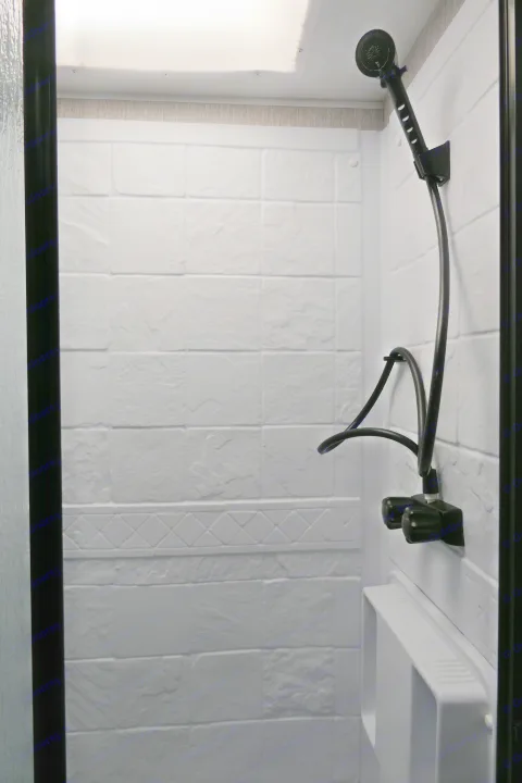 Compact RV rental shower: white textured walls, black showerhead, and a skylight for a bright, functional space.. Coachmen Leprechaun 2021