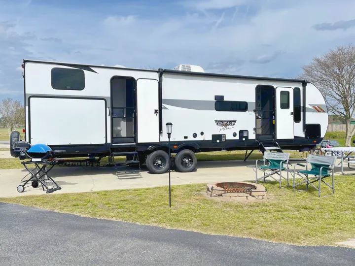 Enjoying the outdoors with an RV rental, complete with a grill, fire pit, and comfy chairs at a sunny campsite.. Forest River Wildwood 32BHDS Platinum 2023