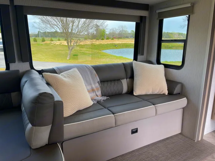 Modern RV rental interior: comfy sofa with pillows, large windows overlooking a scenic pond and trees.. Forest River Wildwood 32BHDS Platinum 2023