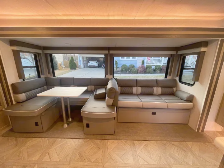 Spacious RV rental interior with a comfortable U-shaped dinette and sofa area, featuring large windows and modern finishes.. Forest River Wildwood 32BHDS Platinum 2023
