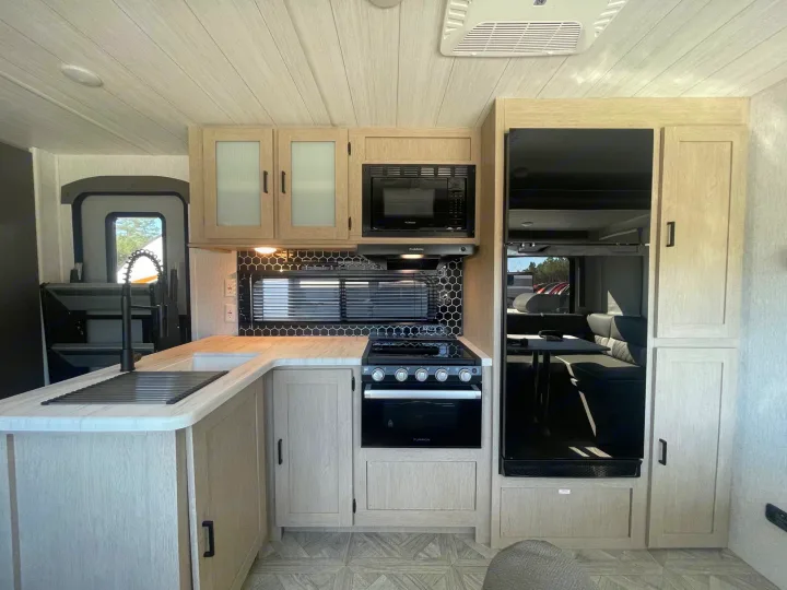 Modern RV rental kitchen with light wood cabinets, black appliances, and a hexagonal tile backsplash.. Forest River Wildwood 32BHDS Platinum 2023