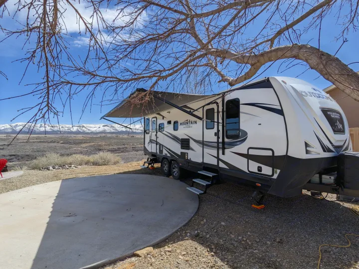 This RV rental boasts an extended awning, concrete patio, and scenic mountain views, perfect for outdoor adventure.. Outdoors RV Timber Ridge 2022