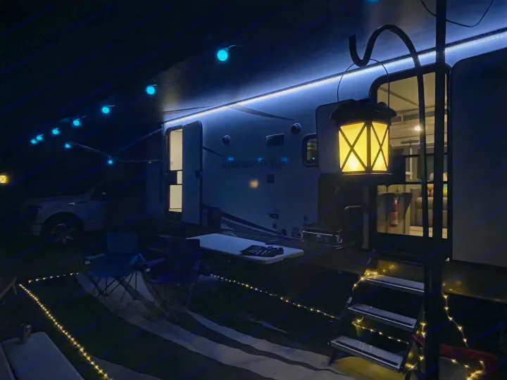 An RV at night, bathed in blue awning lights, a warm lantern, and fairy lights, offering a cozy retreat.. Forest River Salem Hemisphere HL 2021
