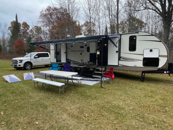 Cozy RV rental travel trailer campsite with an extended awning, outdoor seating, truck, and cornhole boards.. Forest River Salem Hemisphere HL 2021