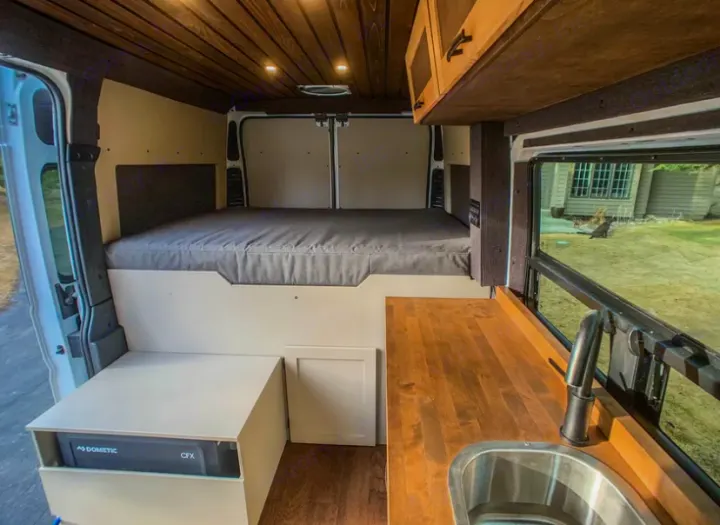 Inside this RV rental: a built-in bed, Dometic fridge, and wood kitchen counter. Ideal camper van setup.. Dodge Ram 1500 2021
