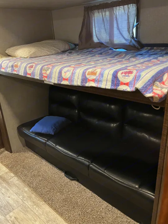 RV rental bunk beds feature a vibrant patterned blanket, a comfortable lower futon, and a blue pillow, perfect for compact sleeping.. Crossroads RV Zinger 2019