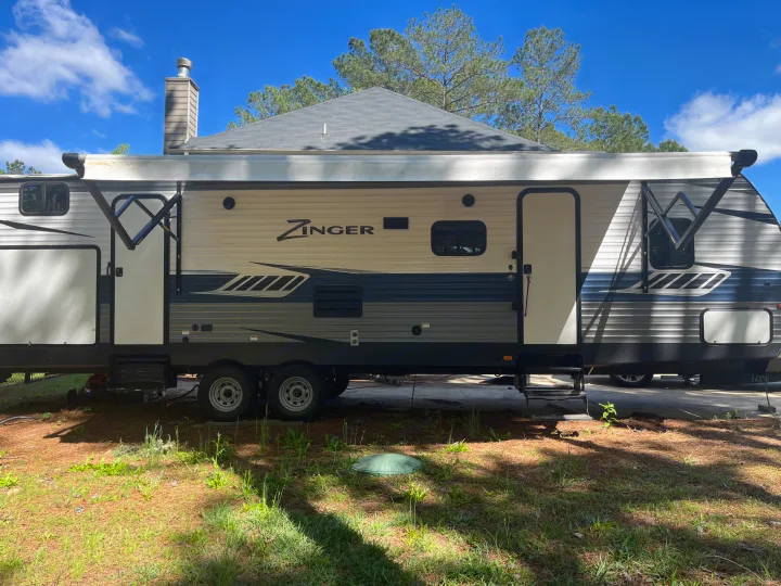 Side view of a Zinger travel trailer, great for rv rental, parked outdoors under blue sky with awning rolled out.. Crossroads RV Zinger 2019