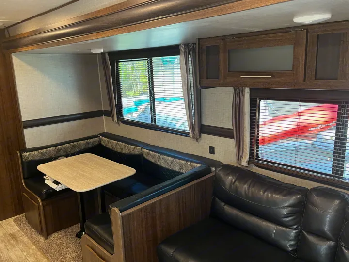 View inside an RV rental showing a modern dinette with a light table, black seating, and a comfortable sofa.. Crossroads RV Zinger 2019