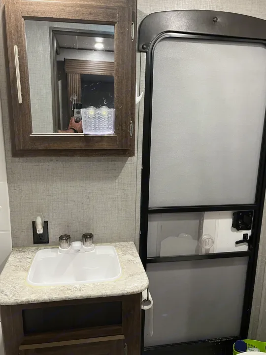 Compact bathroom in an RV rental, showing sink, mirrored cabinet, and adjacent entry door.. Crossroads RV Zinger 2019