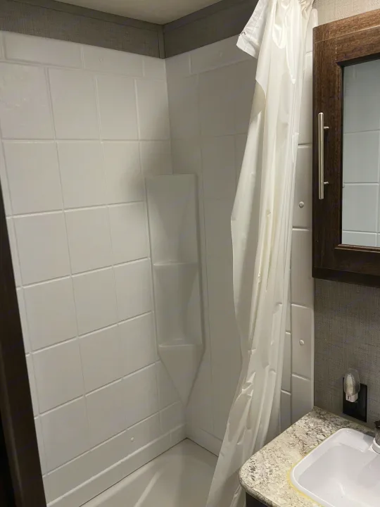 Inside an RV rental, a compact bathroom features a white shower/tub, curtain, and a sink vanity with mirror.. Crossroads RV Zinger 2019