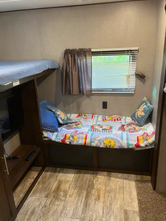 Cozy RV rental interior with bunk beds, a TV, and a lower bed featuring a fun Looney Tunes blanket, ideal for family adventures.. Crossroads RV Zinger 2019