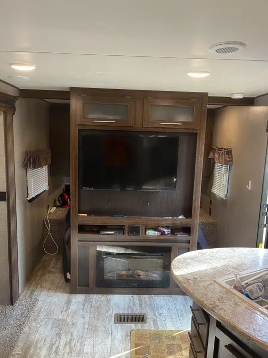 Explore this RV rental's modern living space, featuring an entertainment center with TV, electric fireplace, and kitchen area.. Crossroads RV Zinger 2019