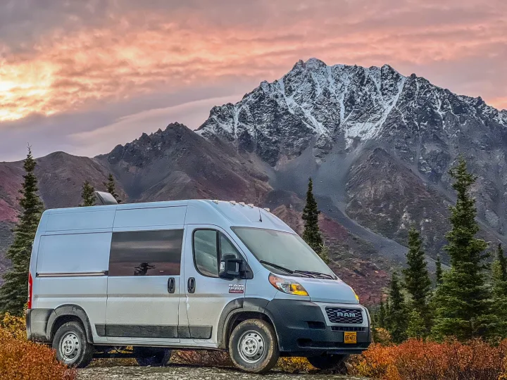White camper van (rv rental) parked in front of snow-capped mountains and autumn foliage under a pink sky.. Dodge Ram 1500 2021