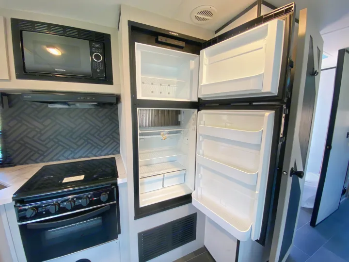 RV rental interior: a clean kitchen with an open Dometic refrigerator, Greystone microwave, stove, and patterned backsplash.. Heartland RVs Mallard 2022