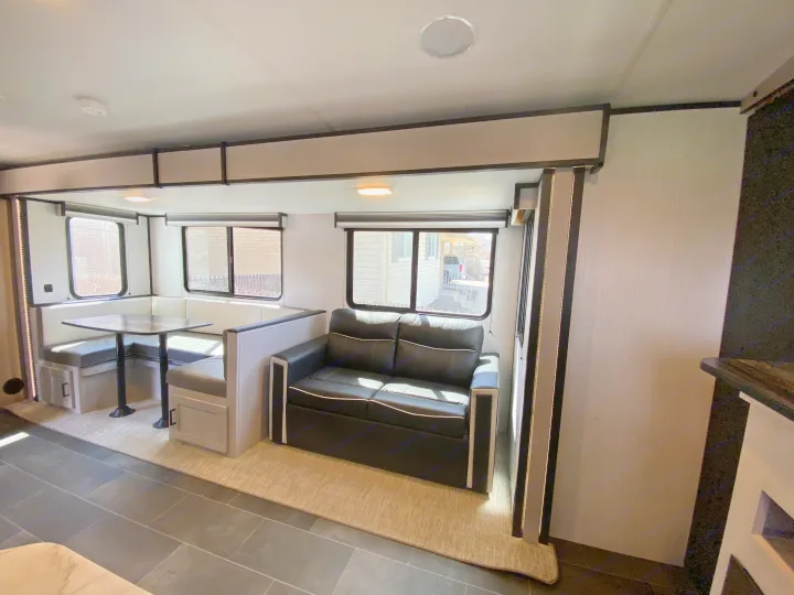 Modern RV rental interior featuring a cozy dinette, black sofa, and ample natural light, creating a comfortable living space.. Heartland RVs Mallard 2022
