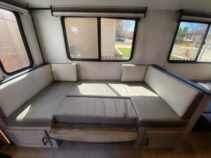 Spacious RV rental interior: a comfy dinette transforms into a bed, offering light-filled seating with exterior views.. Heartland RVs Mallard 2022
