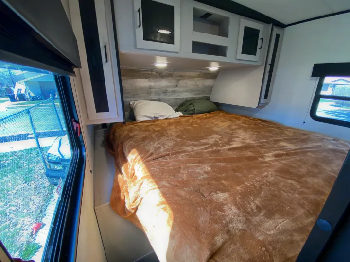 This RV rental bedroom features a cozy bed, overhead storage, and dual windows for natural light and outdoor views.. Heartland RVs Mallard 2022