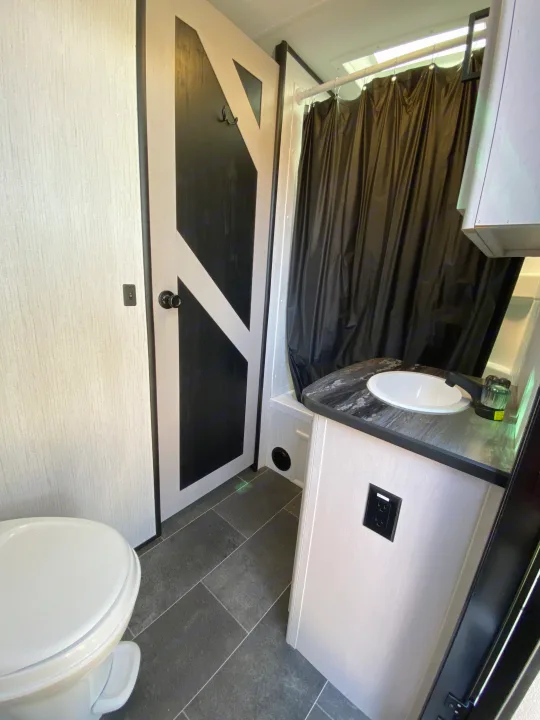Modern RV rental bathroom featuring a toilet, vanity with sink, and shower with a black curtain, showcasing a clean design.. Heartland RVs Mallard 2022