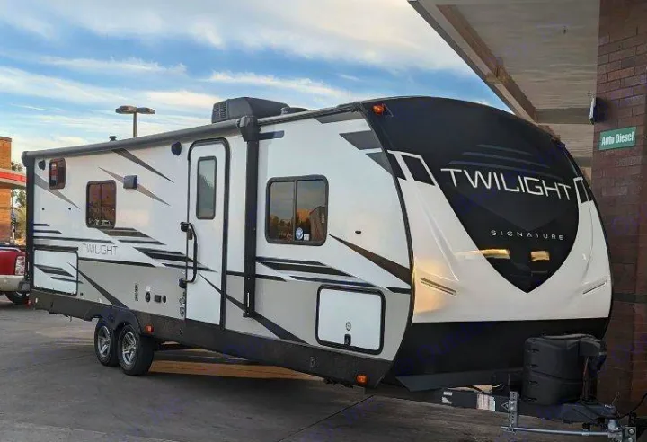 A white and black Twilight Signature travel trailer RV is parked at what appears to be a service station. Explore rv rental options!. Twilight RVS Signature 2022