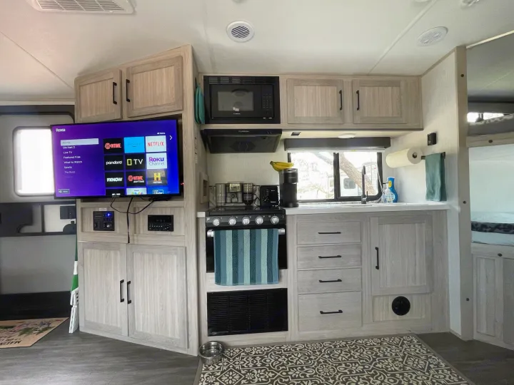 Inside an RV rental: a modern kitchen with TV, microwave, stove, sink, and light wood cabinetry.. Twilight RVS Signature 2022