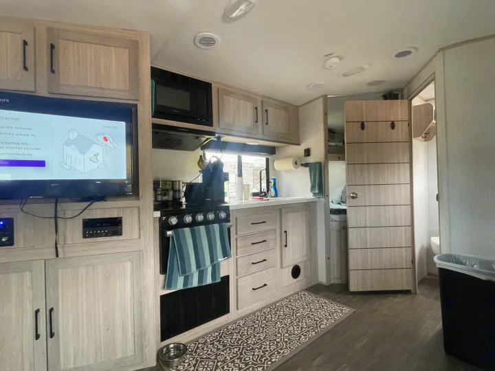 RV rental kitchen & living area with light wood cabinetry, including a TV showing an internet error and a small floor rug.. Twilight RVS Signature 2022