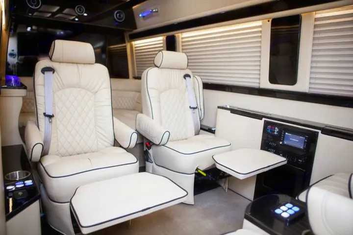 Spacious luxury RV rental interior with cream leather captain's chairs, footrests, and entertainment controls.. Ultimate Toys Ultimate Limo 2022