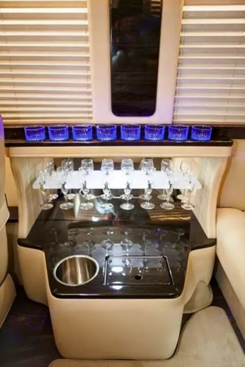 Inside a luxury RV rental: a sophisticated custom bar area with illuminated blue cups, hanging glassware, and a built-in sink.. Ultimate Toys Ultimate Limo 2022