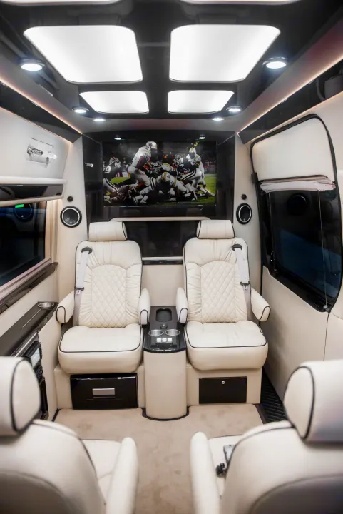 Luxury RV rental: Plush, white leather captain's chairs face a large TV showing football in this spacious interior.. Ultimate Toys Ultimate Limo 2022
