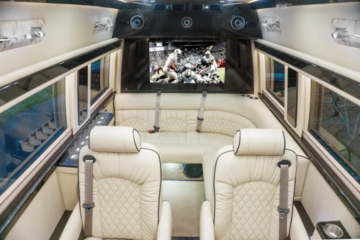 Spacious RV rental interior featuring cream quilted leather seats, a large TV playing football, and sleek amenities.. Ultimate Toys Ultimate Limo 2022
