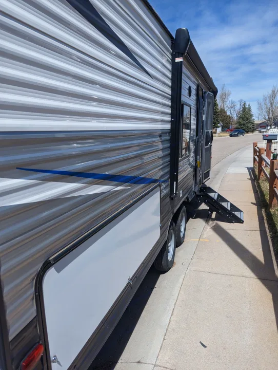 Side view of an RV rental with its open door and extended steps, parked by a sidewalk.. Avenger 26bk 2021