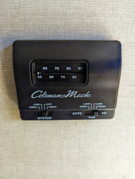 A Coleman-Mach RV thermostat in an rv rental, displaying temperature settings and system/fan modes for climate control.. Avenger 26bk 2021