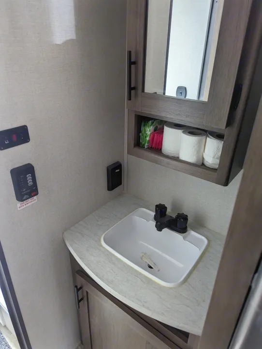 Compact RV rental bathroom: Sink, mirror, toiletries, and winterized tank monitor, ready for your adventure.. Avenger 26bk 2021