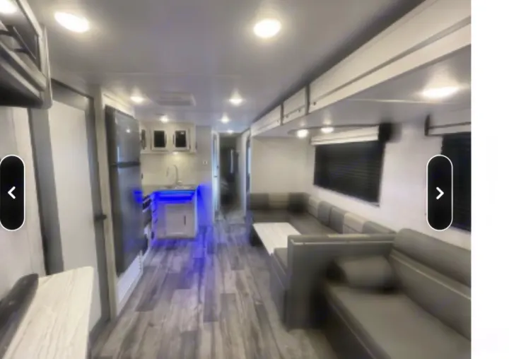 Modern rv rental interior: kitchen with blue lights, U-shaped dinette, wood-look floor, and overhead storage.. Crossroads RV Volante 2021