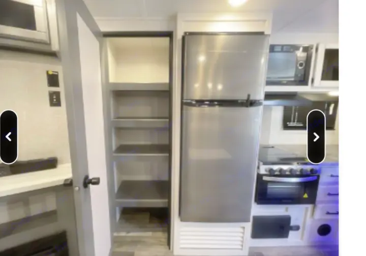 Modern RV rental kitchen with stainless steel fridge, pantry shelves, stove, and microwave for comfortable travels.. Crossroads RV Volante 2021