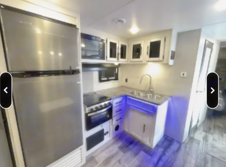 Modern RV rental kitchen featuring stainless steel appliances, white cabinets, and bright under-cabinet lighting with blue accent LEDs.. Crossroads RV Volante 2021