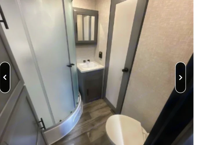 Compact and clean RV rental bathroom with a curved shower, vanity, sink, and toilet in a modern grey and white design.. Crossroads RV Volante 2021