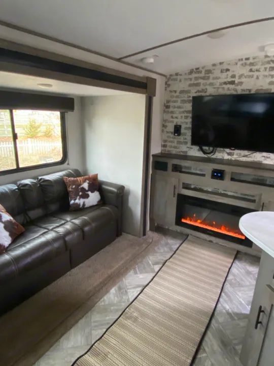 Cozy RV rental living space featuring a comfortable couch, fireplace, TV, and stylish decor.. Keystone Springdale 2021