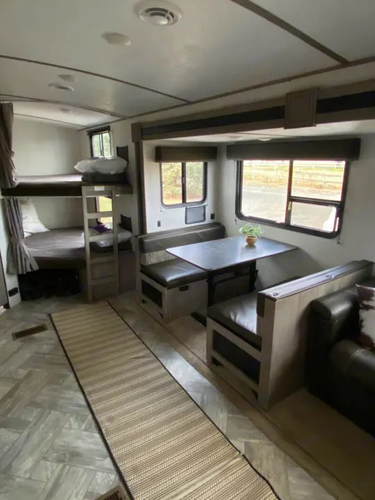 Inside this RV rental: bunk beds, a dinette with a small plant, and a sofa create a comfortable travel accommodation.. Keystone Springdale 2021