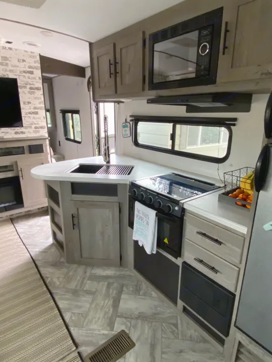 Spacious RV rental kitchen with modern amenities: island sink, stove, microwave, and fridge. Perfect for travel.. Keystone Springdale 2021