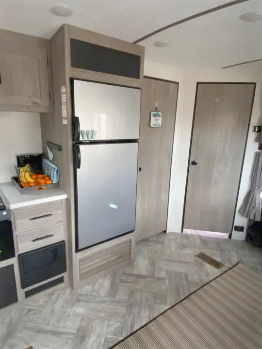 RV rental kitchen featuring a stainless steel fridge, light wood cabinets, and herringbone-patterned floor.. Keystone Springdale 2021
