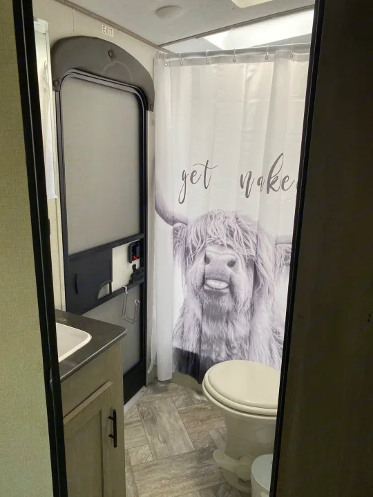 RV rental bathroom with a toilet, sink, and a fun "get naked" highland cow shower curtain.. Keystone Springdale 2021