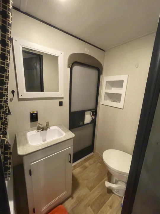 Compact **RV rental** bathroom interior: Features a white vanity, sink, mirror, toilet, and an RV exit door.. Keystone RV Hideout 2022