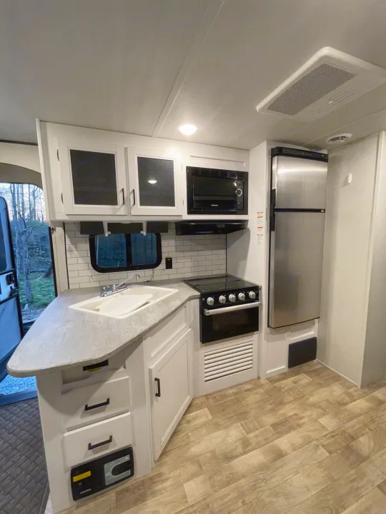 Explore this clean, modern RV rental kitchen featuring a full-size fridge, microwave, stove, and spacious counter with a sink.. Keystone RV Hideout 2022