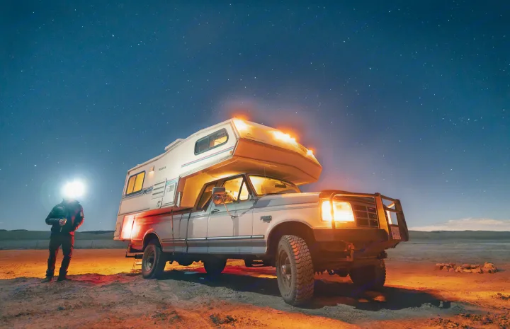 Experience an off-grid night. An RV rental truck camper and a person with headlamp illuminate the desert under a starry sky.. Ford Other 1996