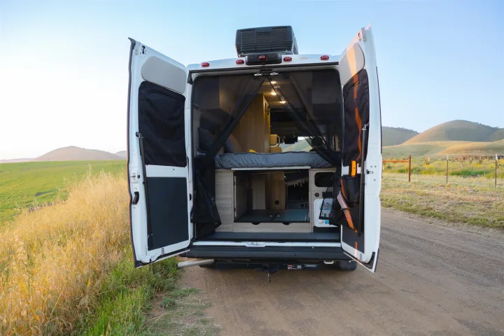 RV rental: Back doors open to a spacious campervan interior with bed & storage, parked by scenic hills. Your road trip adventure awaits!. Winnebago Solis 2022