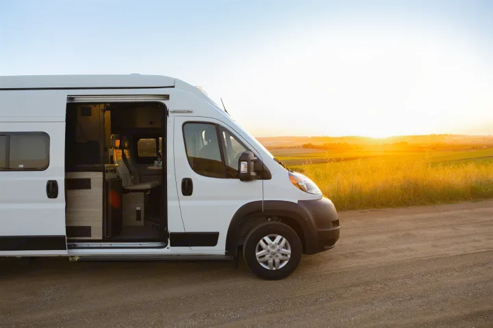 This white RV rental van, door open, reveals its cozy interior at sunset on a dirt road.. Winnebago Solis 2022