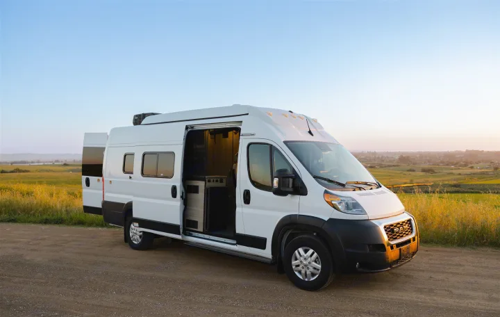 Spacious white camper van rv rental with open doors, parked on a dirt road at sunset. Ideal for outdoor adventures.. Winnebago Solis 2022