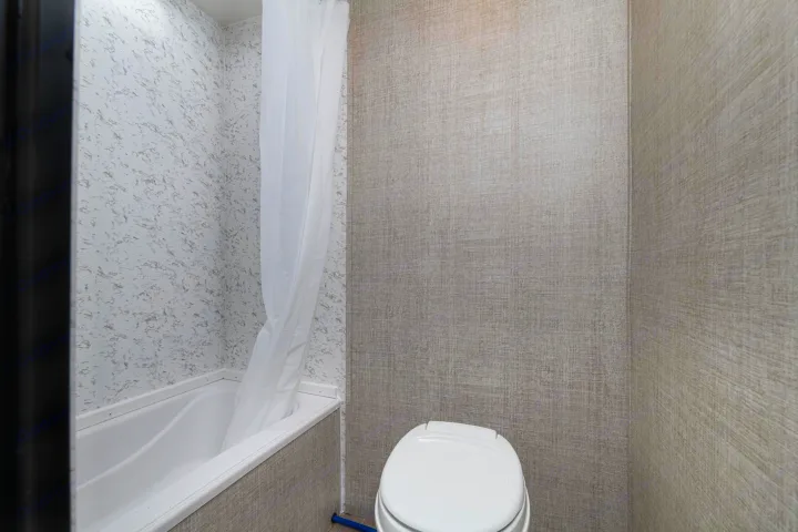 RV rental bathroom with white speckled shower walls, tub, shower curtain, and toilet. Neutral textured walls.. Gulf Stream Ameri-Lite Super Lite 2022