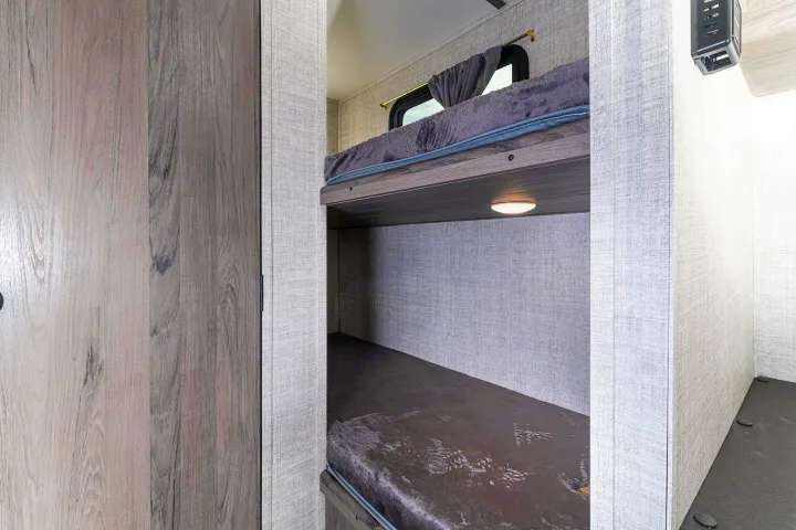 Interior view of an RV rental showing two cozy bunk beds with mattresses, a window, and a reading light.. Gulf Stream Ameri-Lite Super Lite 2022